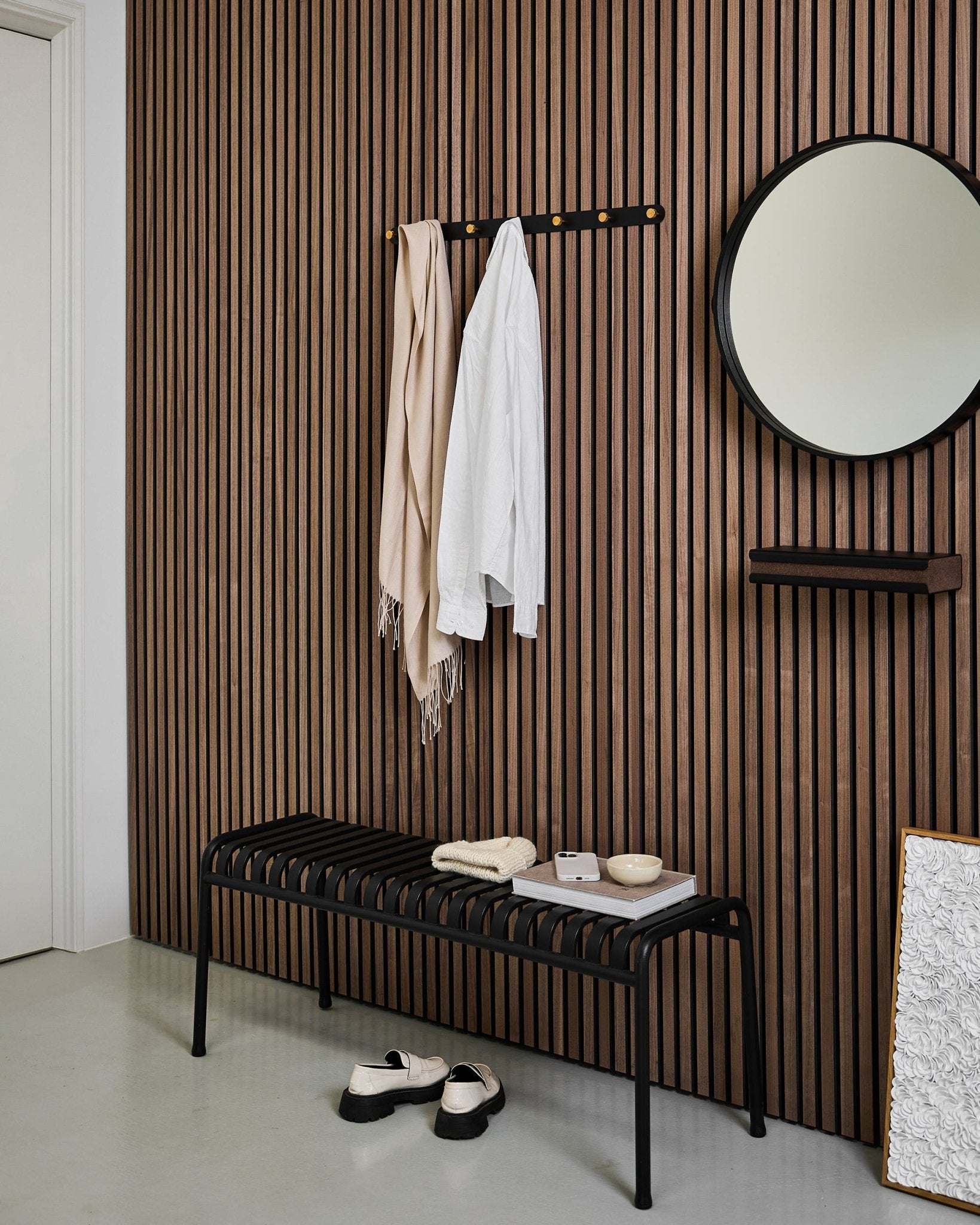 Minimalistisk hall med en WoodUpp Akupanel akustisk ribbvägg, Norr klädkrokslist (Black/Brass, X7), bänk, spegel och modern neutral inredning.